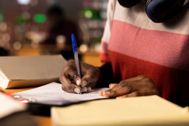 African american college student writes her bachelor degree paper, surrounded by reference books and reliable university study materials. Girl collecting notes and citations for diploma. Close up. clipart