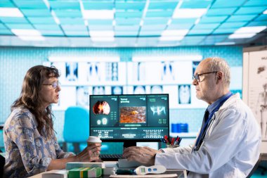 Kıdemli doktor ve hasta modern bir muayenehanede teşhis sonuçlarını tartışıyor. Röntgen ve MRI taramaları yapan bir bilgisayar kullanarak gelişmiş teknolojiyi sergiliyorlar. Bakım yönetimi.