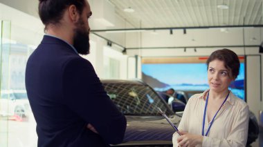 Araba galerisinde soruları cevaplayan bilgili bir satıcı kaliteli müşteri tecrübesi sağlıyor. Yeni araç arayışında müşteriye tavsiye veren bilgili satış elemanı, kamera B