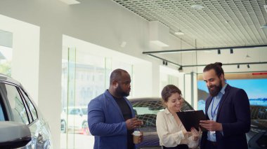 Araba galerisi satıcısı test sürüşünden sonra tatmin olmuş müşterilerin imzalaması için satış sözleşmesi veriyor. Showroom temsilcisi müşterilere satın almaları için ekstra özellikler öneriyor, imza istiyorlar, kamera B