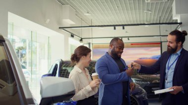 Araba galerisi satıcısı müşterilerle anlaştıktan sonra evrakları ve belgeleri tamamlıyor. Aracın anahtarlarını verdikten sonra müşterilerin imzalaması için satış sözleşmesi veren ajan, kamera B