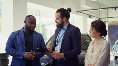 Dost canlısı araba satıcısı müşterilerine satış araçları gösteriyor, özelliklerini ve garantilerini açıklıyor. Müşterinin otomobil seçmesine yardım eden, rekabetçi modelleri karşılaştıran, kamera B