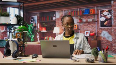 Evdeki ofis masasında çalışan biri klasör dosyalarına bakıyor ve dizüstü bilgisayar kullanıyor, sözleşmeler hazırlıyor. Uzaktan çalışan, defter, kamera B önündeki evrakları kontrol ediyor.