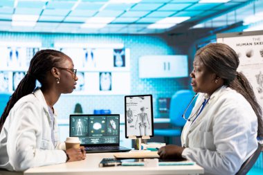 Afrikalı Amerikalı doktor bir kızla sağlık sorunları hakkında konuşuyor, tedavi ve önleme için tıbbi verileri ve teknolojik ekipmanları kullanıyor. Klinik muayene.