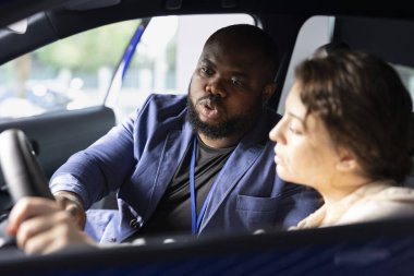 Galeride çalışan bir adam test sürüşü sırasında müşterilere arabalarla ilgili sorulara cevap veriyor. Showroom satış elemanı, araba denemesi yaparken kullanılabilir olan ekstra araba özelliklerini açıklamaktadır