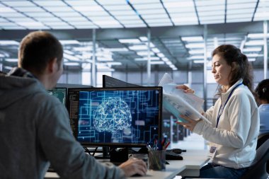 Yönetici, endüstri standartları ve düzenleyici gereksinimlere uyduğundan emin olmak için makine öğrenme sunucu çiftliğinde evrakları inceliyor. Veri merkezi güvenlik protokollerini denetleyen denetleyici