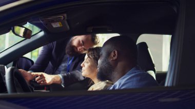 Showroom satıcısı test sürüşünü bitirdikten sonra müşterilerine tablet üzerinde satın alınabilir ekstra araba özellikleri gösteriyor. Satış temsilcisi, araç addons kataloğunu cihaz B 'de karı kocaya gösteriyor.