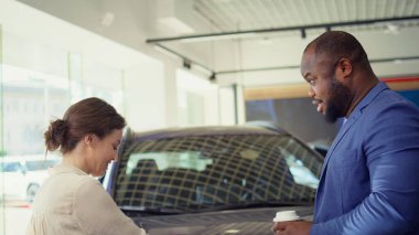 Müşteriler araba galerisine geliyor, müşterilere uygun araçları sergilemeye hazır dost bir araba satıcısı tarafından karşılanıyorlar. Galeride yürüyen müşteriler, temsilci ve kamera B tarafından karşılanıyorlar.