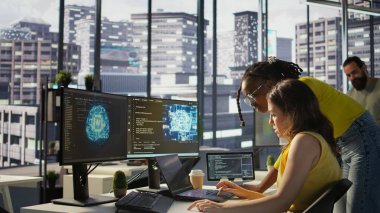 Büyük ölçekli makine öğrenme modellerini eğitmek için bulut hesaplama kaynaklarını kullanan iş arkadaşının yardımıyla. Kadın ve iş arkadaşı, Yapay Zeka şirketini bilgisayar, kamera B kullanarak izliyor.