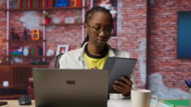 Tabletteki sosyal medyaya bakmak için işten izin alan bir kadın. Apartman ofisindeki uzaktan çalışan, sosyal ağ uygulamasını cihazda kullanmak için görevleri duraklatıyor, kamera B