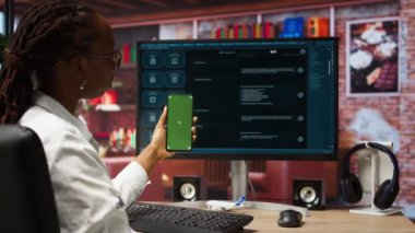 Masada oturan kadın, modern şehir merkezindeki AI LLLM sohbet robotu yazılımı ve yeşil ekran telefon kullanıyor. Apartman dairesi, kamera A 'da bilgisayar ve akıllı telefon üzerinde büyük bir dil programı kullanıyor.