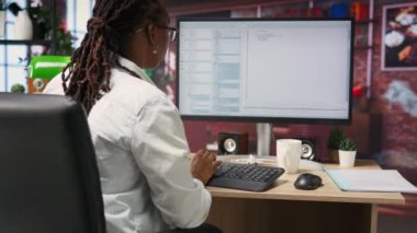 İş istasyonundaki programlamada kodlayıcı, kod satırları yazmak, geliştirme araçları kullanmak, stres hissetmek. Ofisteki kadının son teslim tarihi var, hata ayıklama yazılımını bitirmek için stresli, kamera B