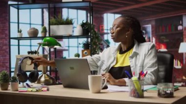 Kadın, şirket projesi için veri ararken müzikten zevk alıyor. Kişisel ev işlerinde çalışıyor. Teleworker dizüstü bilgisayarın önünde oturuyor ve kulaklık ve kamera A kullanıyor.