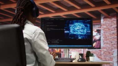 Yapay zeka sinirsel ağlarının bakımını yapan yönetici bilgisayarlı model, müzik dinliyor. Kulaklık takan teknik destek uzmanı yapay zeka sistemlerini ve kamera A 'yı kontrol ediyor.