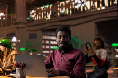 Siyahi erkek öğrenci kampüs kütüphanesinden akademik bilgi topluyor, sınav hazırlıklarına yardım etmek için araştırma yapıyor. Eğitim fırsatı olan genç bir öğrenci sertifika için savaşıyor..