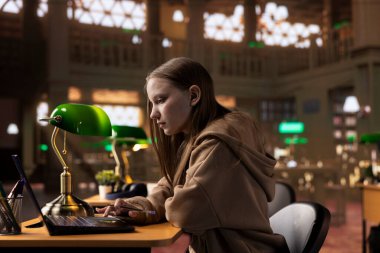 Üniversite kütüphanesindeki akademik dersleri için notlar toplayan, sınav hazırlıkları yapan ve diploma projesi üzerinde çalışan bir kız öğrenci. İhbar arayan genç yetişkinler.