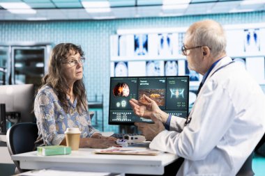 Tıbbi uzman muayenede oksijen seviyesi doygunluğunu ölçmek için profesyonel araç kullanıyor, parmak üzerinde oksimetre kullanıyor ve klinikteki yaşlı kadına danışıyor. Sıhhiye nabız oranı ölçümü yapıyor.