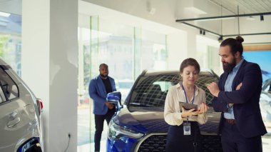 Satıcı kadın, tablet kullanarak adama seçenekler sunuyor. Satın alması için onu etkilemeye çalışıyor. Showroom temsilcisi, aygıt, kamera B 'de ayrıntıları gösteren, istemciye uzatılmış garanti sunar