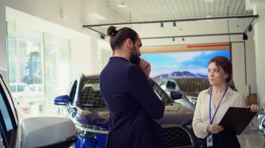 Satış elemanı müşteriyle konuşuyor, satın alma kararlarını neyin etkileyebileceğini anlamak için araç tipi, marka ve fiyat aralığını kavramaya çalışıyor, kamera B