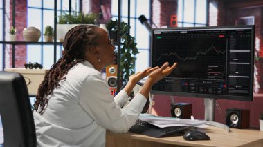 Hüsrana uğramış borsa simsarı üzgün, düşen hisse senedi fiyatlarını, kırmızı çizelgeleri ve kayıpları gösteren bilgisayar ekranlarına bakıyor. Yatırımcı, borsa hisselerindeki düşüşe bakarken baskı altında.