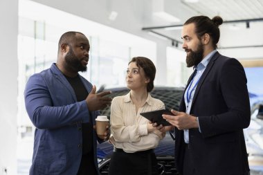 Araba satış müdürünün müşteriye tablet kullanarak satış araçları göstermesi, karakteristik özellikleri açıklıyor. Showroom satıcısı dijital aygıt kullanarak, modelleri karşılaştırarak müşterinin otomobil seçmesine yardım ediyor