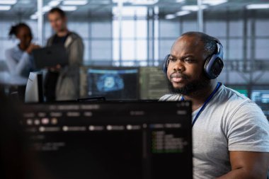 Sunucu merkezinde müzik dinleyen bir mühendis, enerji tüketimini azaltmak için güç yönetimi çözümleri uyguluyor. Kulaklık takan, şarkı duyan ve veri merkezine yeni sistemler entegre eden bilişim uzmanı