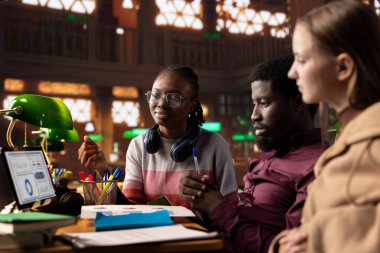 Üniversite öğrencileri kampüs kütüphanesinde uluslararası işletme yönetimi ve yönetimine odaklanan bir girişim projesinde işbirliği yapıyorlar. Akademik diplomaları için sıkı çalışıyorlar..