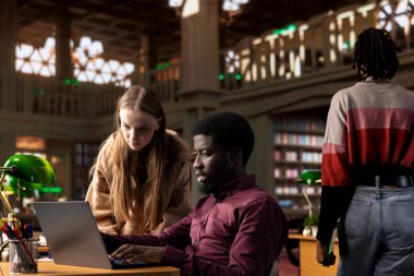 Kampüs kütüphanesinde bir takım projesi üzerinde çalışan çok ırklı öğrenciler akademik veritabanına ve çeşitli kitaplarla araştırma koleksiyonuna danışıyorlar. Genç yetişkinler yüksek notları garanti ediyor.
