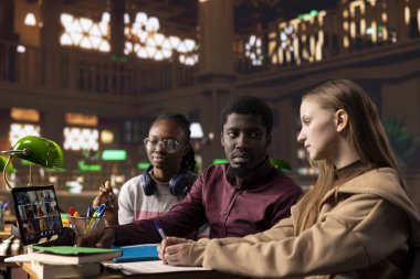 Genç bir grup öğrenci, üniversite kütüphanesinden gelen çevrimiçi konferans derslerine katılarak, tablet üzerine uzak bir webinar kursuna katılıyorlar. Çeşitli insanlar akademik öğretmenden öğreniyor.