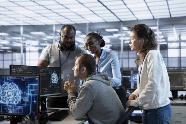 Teknisyenlerle ekip toplantısı yapıyor, yüksek teknoloji veri merkezinde görevler veriyor. Denetmen, BT uzmanlarıyla beyin fırtınası yapıyor. Onlara yapay zeka süper bilgisayarlarını nasıl izleyeceklerini söylüyor.