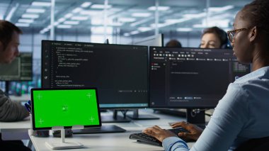 Bilgisayarlarda kod yazan ve ekipmanları güncelleyen bilişim destek çalışanları önünde izole edilmiş ekran tableti. PC masasındaki mühendisler sunucu kümelerini krom anahtar aygıtı, kamera B kullanarak denetlerler.