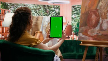 Ressam, resim atölyesinde, yağlı boya resimli bir başyapıta bakan, izole edilmiş bir maket ekranlı bir cihaz tutuyor. Güzel bir sanat galerisi için güzel bir kırsal sanat eseri, yaratıcılık. Kamera B.