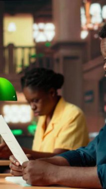 Dikey Video Üniversitesi öğrencisi, dersleri gözden geçirmek ve ders materyallerini düzenlemek için klasik çalışma alanını kullanarak geleneksel bir kütüphanede akademik konuları araştırmaktadır. Sınavlar için sınıf notları tamamlanıyor