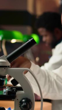 Dikey Video Üniversitesi öğrencisi mikroskop altında hücre ve mikroorganizmaları araştırarak sınava hazırlanıyor. Üniversite kütüphanesindeki akademik veritabanındaki kitap ve belgeleri kullanarak. Kamera A.