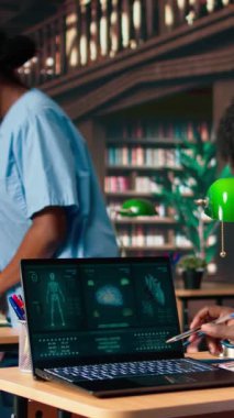 Dikey Video Tıp Fakültesi öğrencisi anatomi araştırma kağıtlarından kişisel notlar alıyor ve tıp kariyeri için sağlık yöntemlerini inceliyor. Kampüs veritabanındaki kitapları kullanan bir erkek öğrenci. Kamera A.