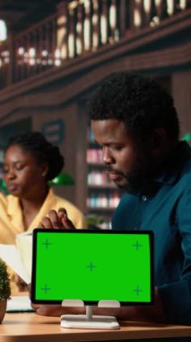 Dikey Video Afrikalı Amerikalı öğrenciler akademik veritabanından yeşil ekranın yanındaki araştırma kağıtlarına danışarak fotokopi kitaplarından bilgi alıyorlar. Kütüphanedeki genç öğrenci takımı. Kamera A