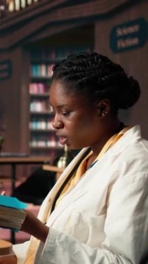 Dikey Video Siyah tıp öğrencisi kampüs kütüphanesinde sağlık kitapları okuyor, kadın tıp sınavlarını geçmek ve kariyer yapmak için araştırma yapıyor. Bayan öğrenci vaka dosyaları üzerinde çalışıyor