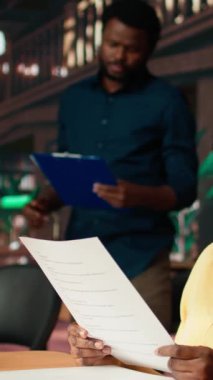 Üniversite kütüphanesi masasında notlar ve kağıtlarla birlikte derslerine dalmış, sınav hazırlıkları için akademik veritabanına danışıyor. Bilgi ve kendini geliştirme