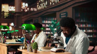 Mikroskop analizi sırasında virüs araştıran erkek öğrenci ve klasik bir kütüphanede akademik okuma. Tıp fakültesi öğrencisi biyolojiye ve sınav hazırlıklarına olan bağlılığını yansıtıyor. Kamera A.
