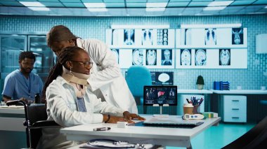 Siyahi hekim steteskop kullanarak hastasına danışmanlık yapıyor. Akciğerleri ve kalp atışlarını dinliyor. Rutin solunum kontrolünde servikal köpüklü tekerlekli sandalye kullanıcısı. Kamera B.