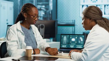 Rutin kontrol sırasında oksimetre kullanarak oksijen doygunluğunu ve nabız oranını ölçen bir sağlık uzmanı, modern tıbbi aletlerle siyah bir kıza danışın. Hayati belirtiler ölçülüyor. Kamera A.