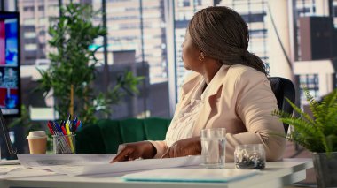 İşletme sahibi, ofis alanları üzerine planlar üzerinden stratejik araştırmalar yürütüyor, yeni bir yaratıcı çalışma alanı oluşturmak ve düzenlemek için planlar kullanıyor. CEO ofisin yerini değiştirmekle ilgileniyor. Kamera B.