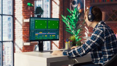 Video düzenleyici, video montajı yaparken kullanılacak anahtar çerçeveleri seçiyor, yeşil ekran bilgisayarda evden çalışıyor. B kamerasındaki krom anahtar bilgisayardaki film görüntülerini düzenlemek için fareyi kullanan adam.