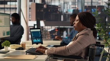 Finansal strateji üzerinde çalışan, organizasyonel amaçlara ulaşmak için veri analizlerini gözden geçiren Afrikalı Amerikalı bir çalışan. Kadın analist maluliyet dostu bir ofiste çalışıyor. Kamera A.