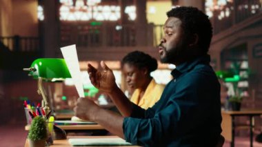 Üniversite öğrencisi kampüs kütüphanesinde ders çalışmak için çırpınıyor, bunalmış bir öğrenci endişeyle öğrenmeye çalışıyor. Erkek ergen notlarıyla ilgileniyor. Kamera B.