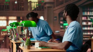 Siyahi tıp fakültesi öğrencileri kütüphanede anatomi kitapları ve ders notları okuyor çalışma grubu öğrenme seansı. İnsanlar tıp kariyeri için sınav hazırlıklarına odaklanıyor. Kamera B.