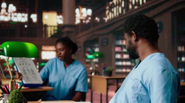 Afrika kökenli Amerikalı öğrenciler, tıp fakültesi sınavları için birlikte çalışıyorlar, kadın ve erkek birbirlerine sağlık hizmetleri detaylarını ezberlemede yardım ediyorlar. Öğrenciler kütüphanede tıbbi araştırmalara odaklanırlar. Kamera A.