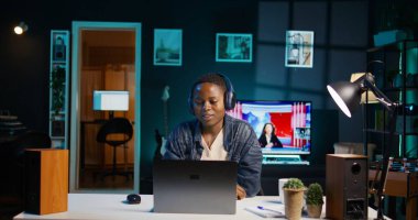 Neşeli kadın, dizüstü bilgisayarında kulaklık kullanarak televizyon izleyerek evde dinleniyor. Mutlu insan dairede boş vakit geçirmekten zevk alıyor, eğlence medyası içeriği tüketiyor, kamera B