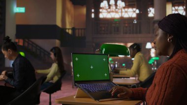 Sessiz bir kütüphane çalışma alanında dizüstü bilgisayarında yeşil ekranla yazı yazan siyahi kendine güvenen kütüphaneci, kaynakları organize ediyor ve öğrencilere akademik yolculuklarında gurur ve uzmanlıkla akıl hocalığı yapıyor. Kamera A.