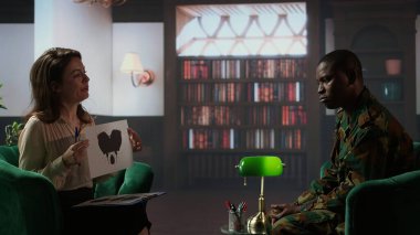 Danışman uzman psikanaliz sırasında askeri üniformalı bir askere Rorschach mürekkep lekesi testi sunar. Kitap raflarıyla dolu sıcak bir ofiste terapi gören farklı insanlar. Kamera A.